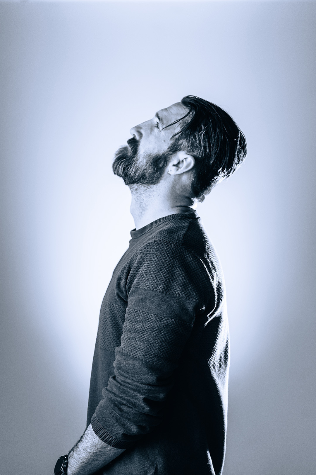 Portret van een man met baard en bril die omhoog kijkt, gefotografeerd met koel blauw licht voor een serene en introspectieve sfeer.