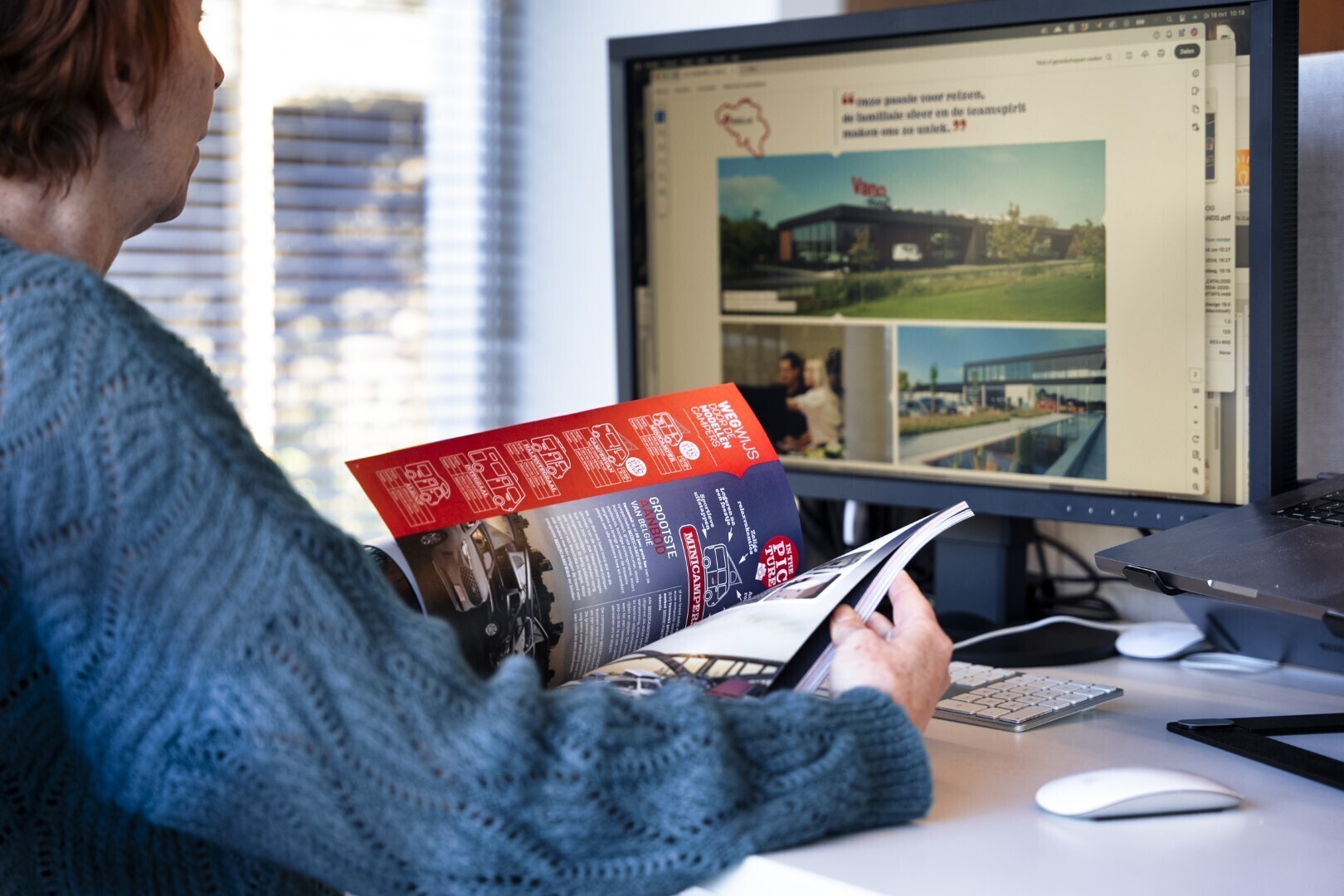 Foto van een vrouw die aan het bladeren is door een magazine en aan het kijken is naar een computerscherm