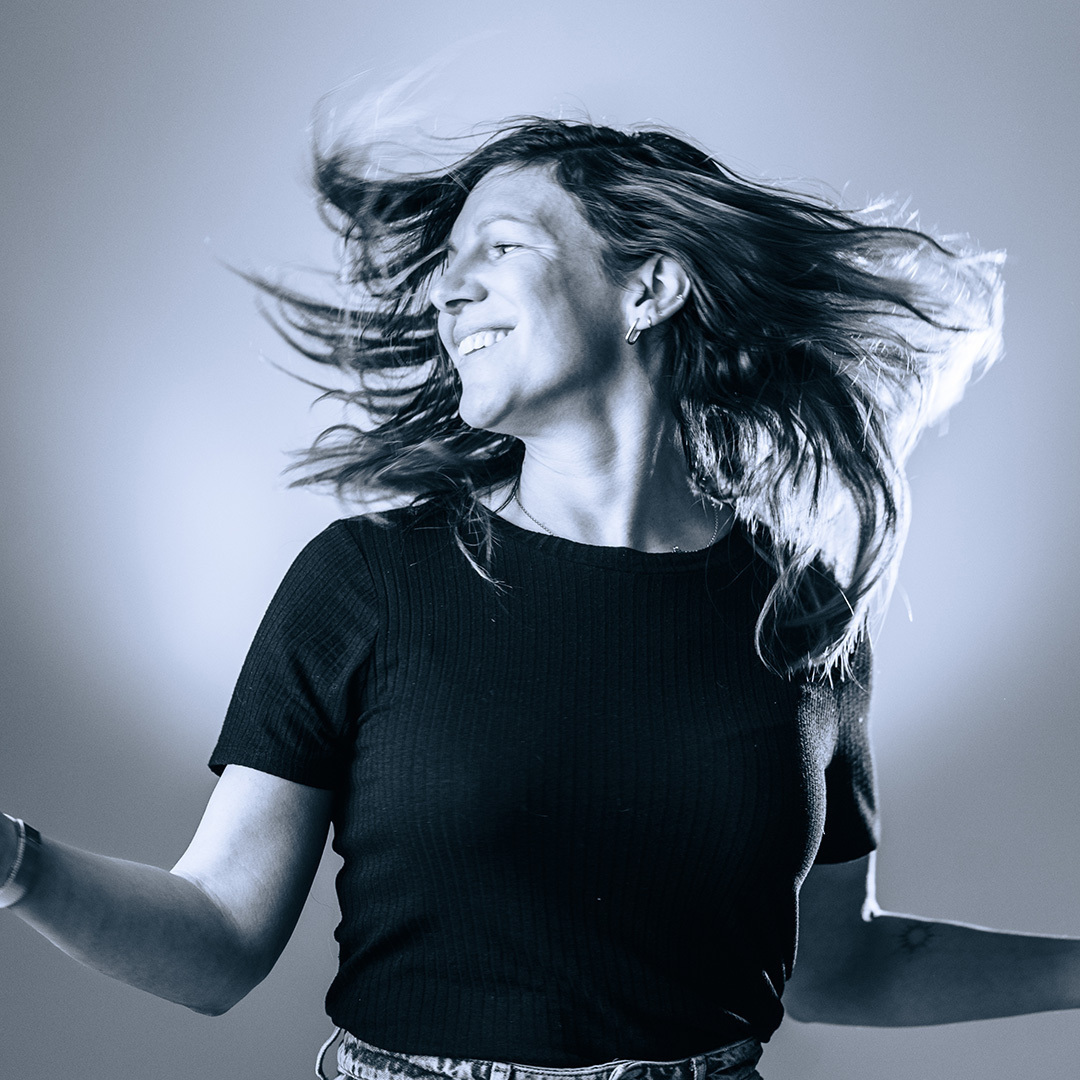 Zwart wit foto van vrouw met lang haar in beweging, lachend en dansend, gekleed in een zwarte top