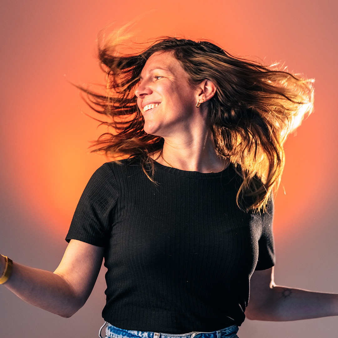 Zwart wit foto van vrouw met lang haar in beweging, lachend en dansend, gekleed in een zwarte top