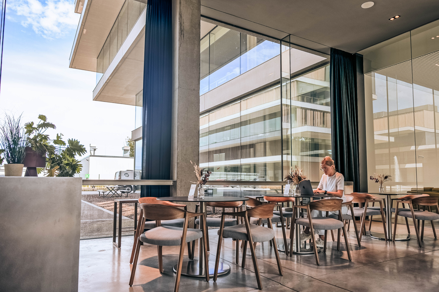 Moderne horecaruimte met glazen wanden en een vrouw die alleen aan een tafel zit.